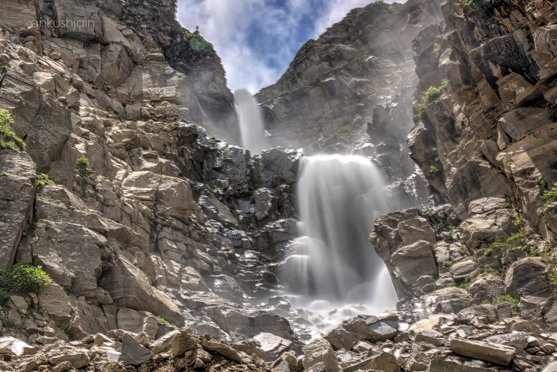 A thin waterfall cascading down a sheer rock face onto scree below